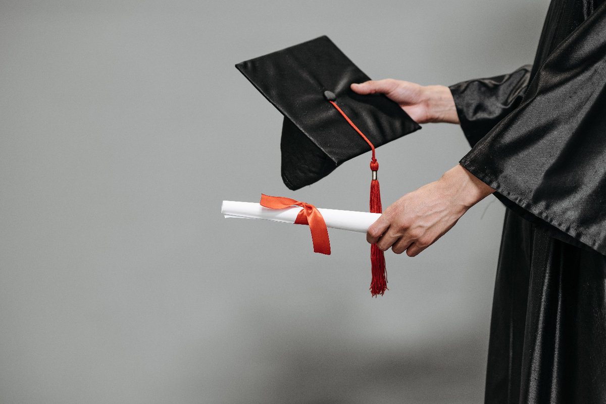 Someone in a graduation gown holds a cap and diploma in their hands.